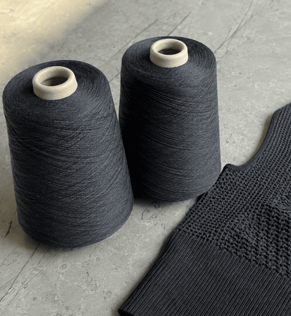 Two cones of charcoal performance yarn beside a finished seamless knit garment